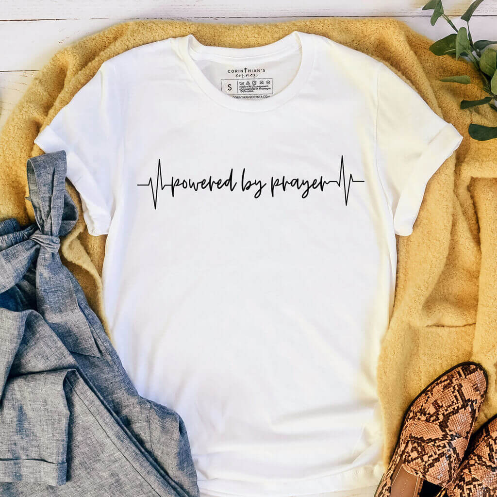 Simple white t-shirt with EKG design that reads "powered by prayer"
