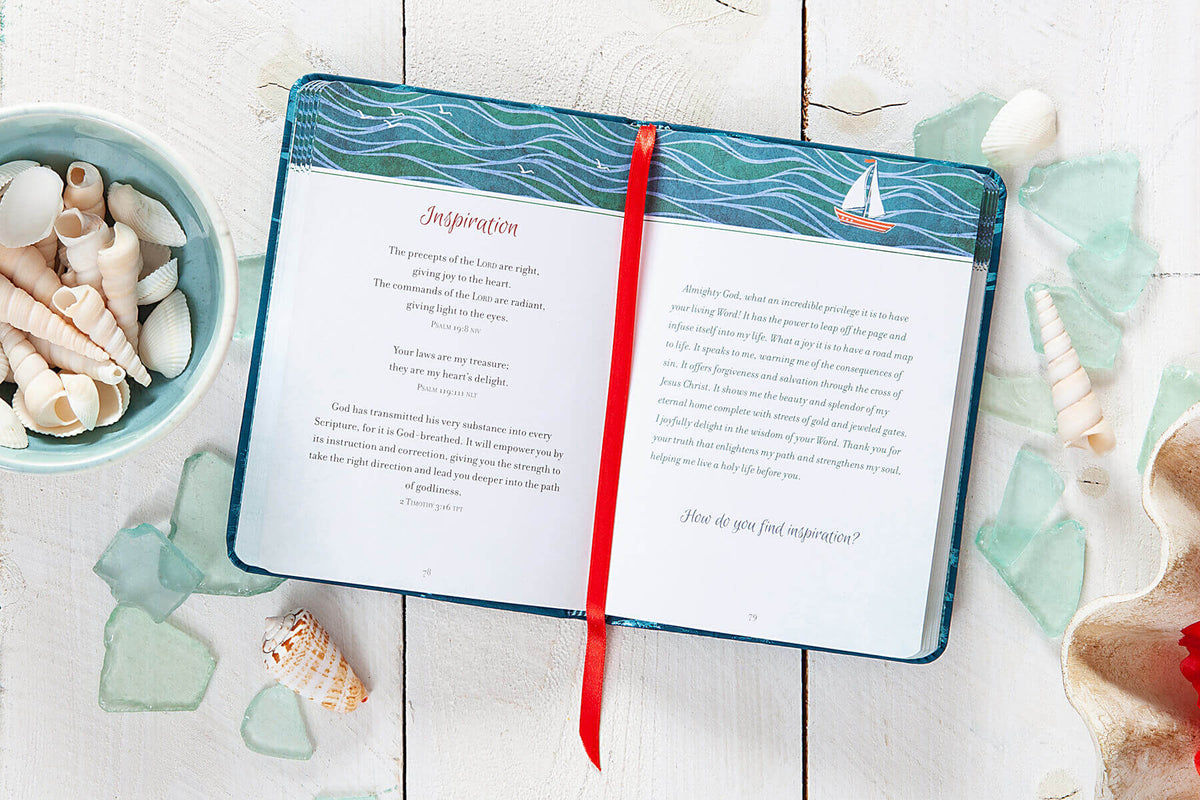 Open book with a red bookmark on a wooden surface surrounded by seashells and decorative items.
