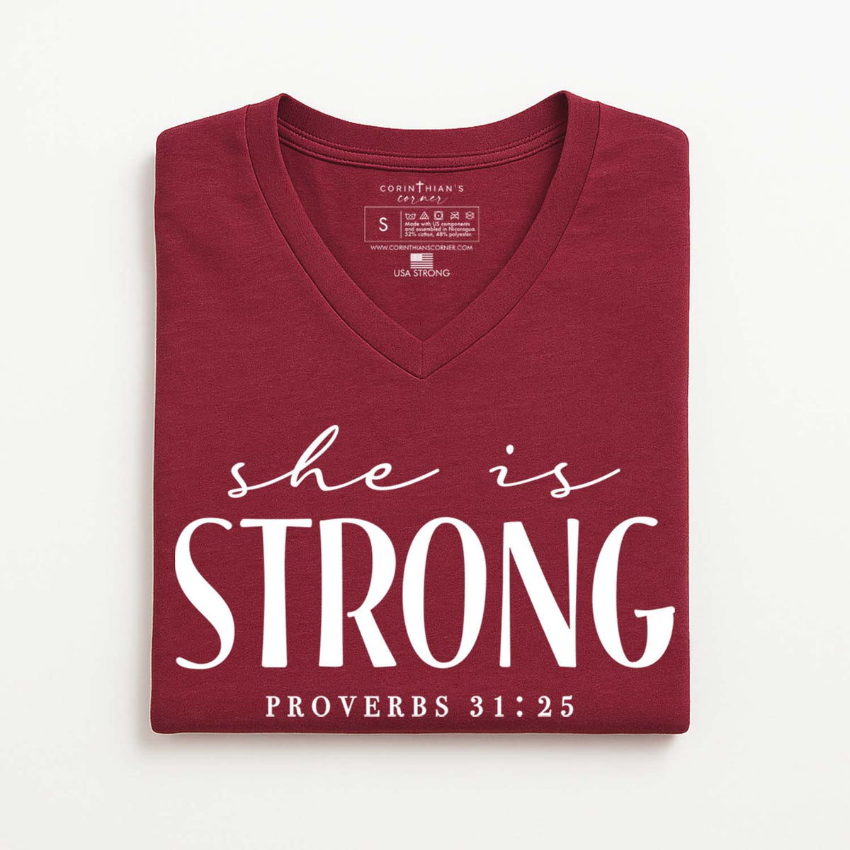 Folded maroon t-shirt with 'she is STRONG Proverbs 31:25' text on a white background