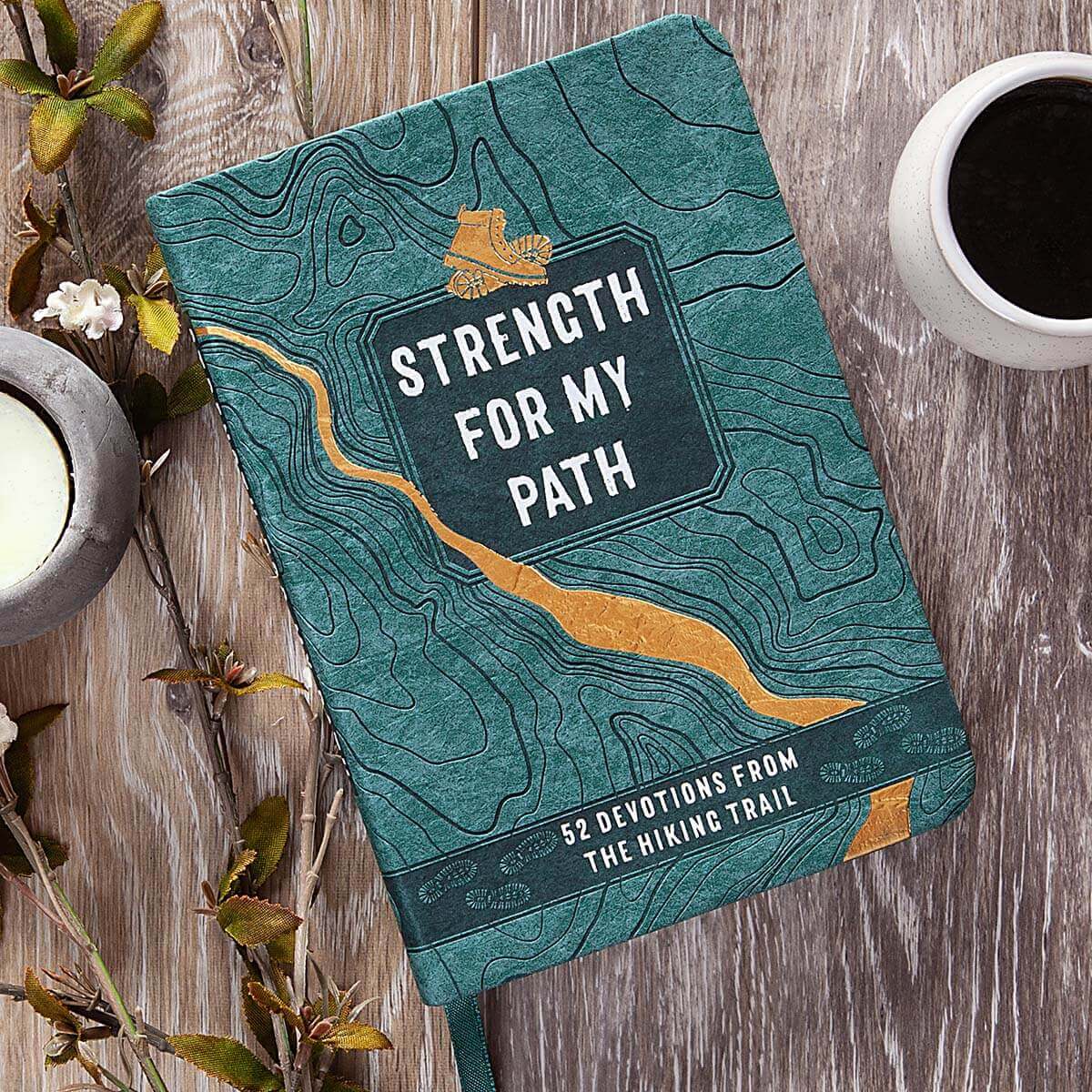 Book titled 'Strength for My Path' on a wooden surface with a cup of coffee and candle.
