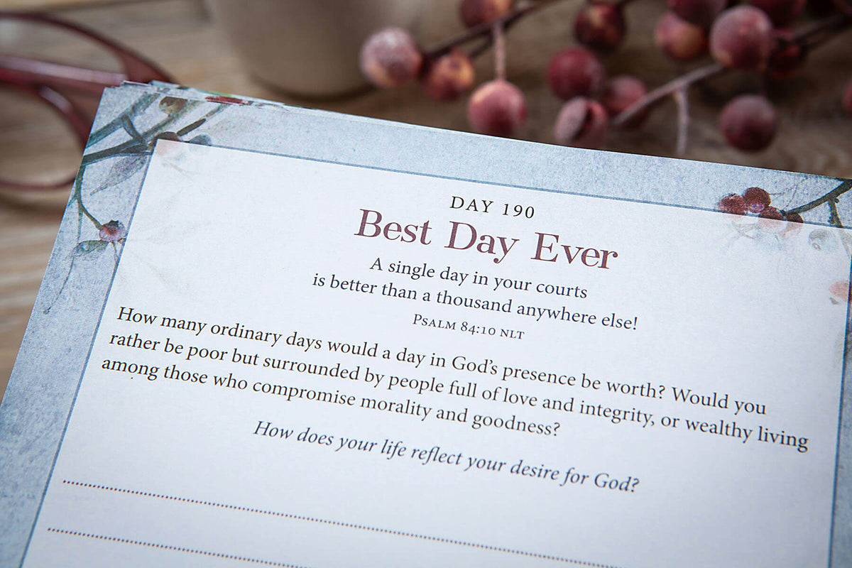 A printed card or booklet page titled 'Best Day Ever' with inspirational text and a line for writing, photographed on a soft floral surface with blurred berries in the background.