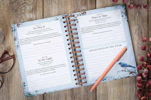 An open spiral-bound journal or planner spread on a wooden surface, showing printed pages titled 'No Plan B,' 'Peace Is Mine,' and 'Reflections of the Week,' with a peach pen resting on the right page. Decorative glasses and red berries are partially visible around it.