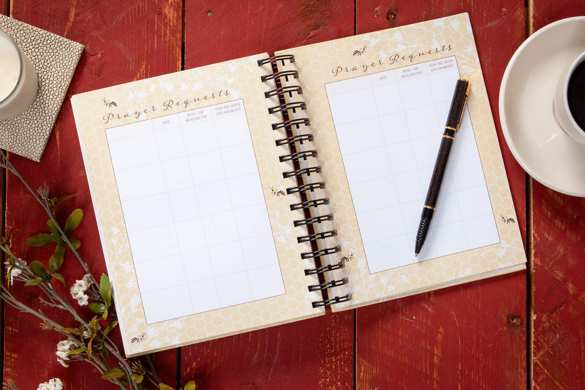 Open notebook with prayer requests on a red wooden surface with a pen and coffee cup.
