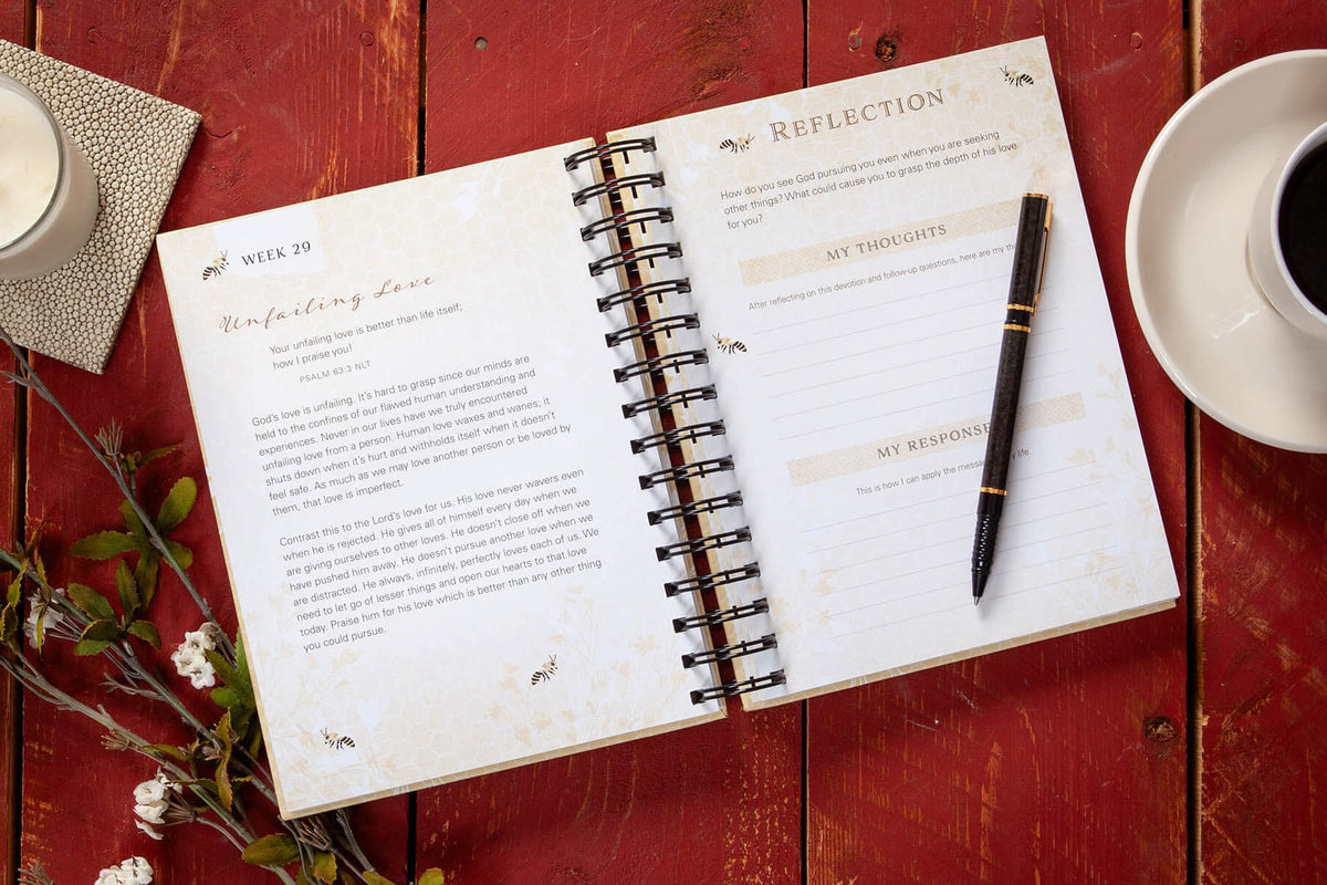Open spiral-bound notebook with a pen on a red wooden surface with a cup of coffee and decorative elements.