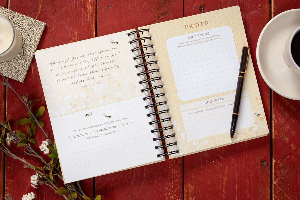 Open journal with prayer pages on a wooden surface with a cup of coffee and branches.