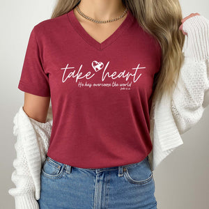 Person wearing a maroon t-shirt with 'take heart' text and design, standing against a neutral background