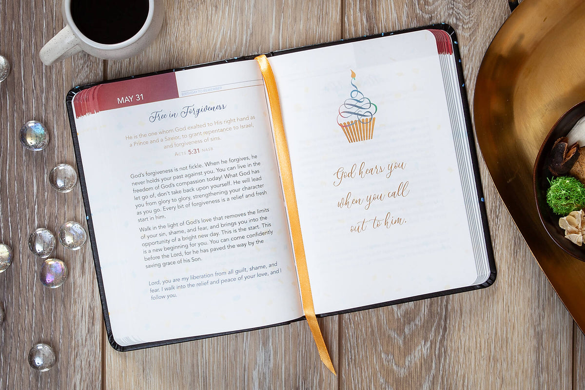 Open devotional with a decorative page on a wooden surface with a cup of coffee and decorative items.