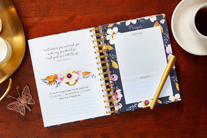 Floral planner on a wooden surface with a pen and cup of coffee
