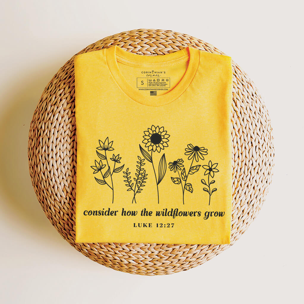 Bright yellow tee with the Biblical passage Luke 12:27 and a collection of beautiful wildflowers
