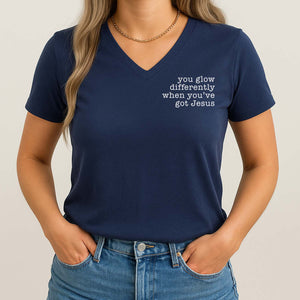 Woman wearing a navy blue t-shirt with text 'you glow differently when you've got Jesus' on a plain background