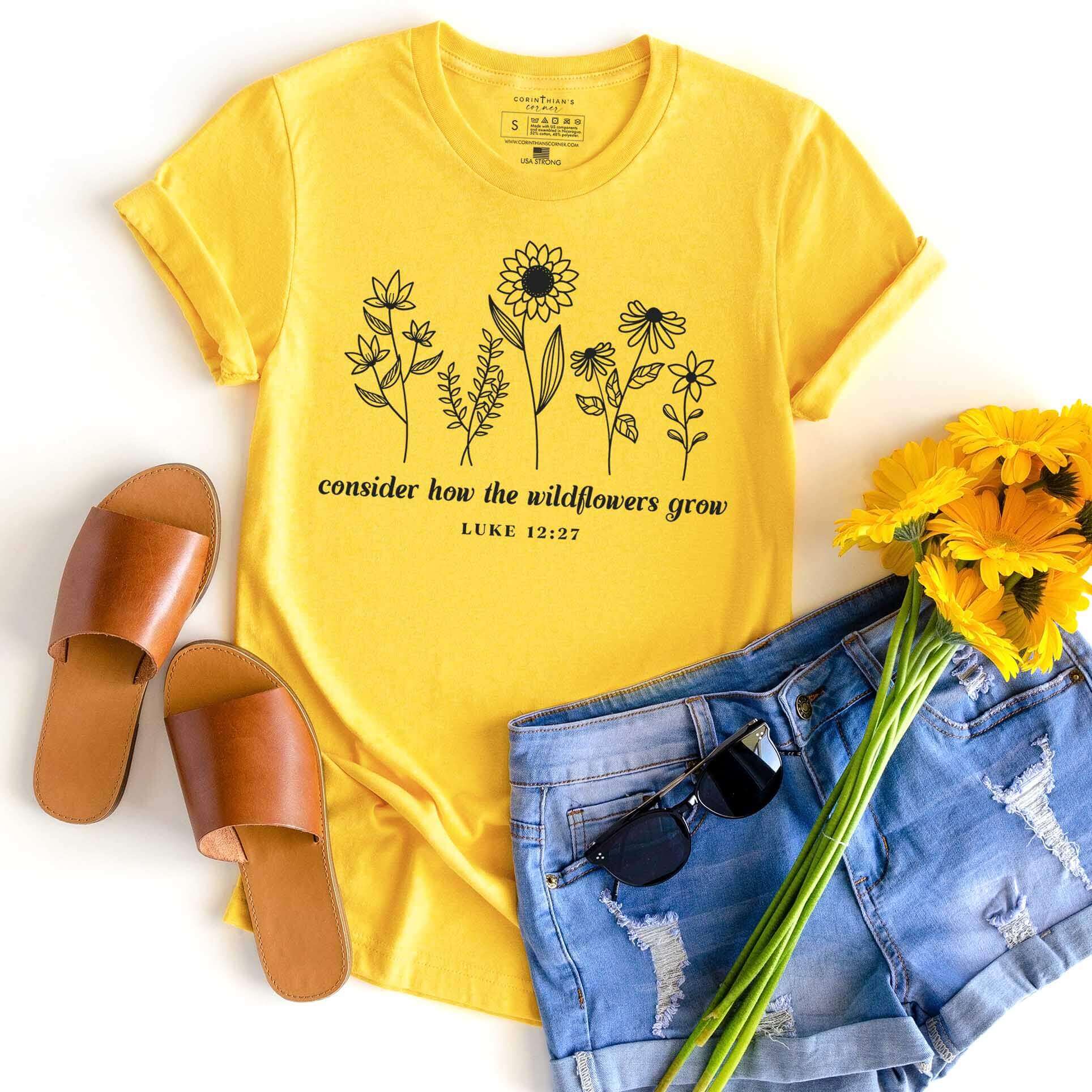 Bright yellow tee with the Biblical passage Luke 12:27 and a collection of beautiful wildflowers