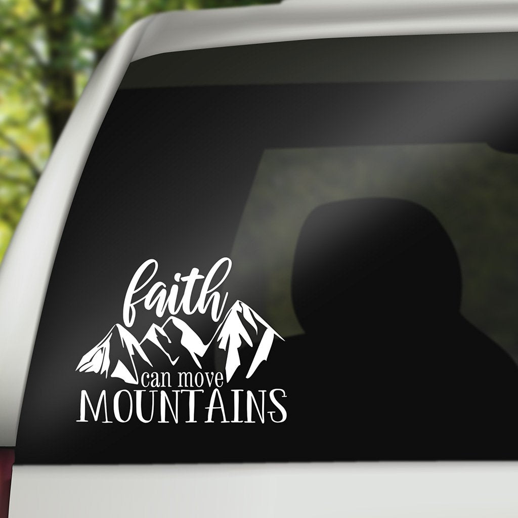 White decal on the back of an SUV with a mountain range design and text reading "faith can move mountains"