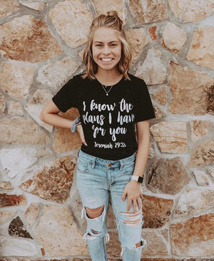 Young woman smiles with hand on her hip wearing black Christian t-shirt
